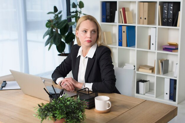 Empresaria joven rubia que se sienta en el lugar de trabajo en la oficina