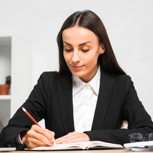 Empresaria joven sonriente que escribe notas del diario con el lápiz