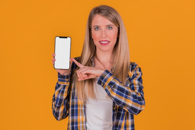 Empresaria joven sonriente que señala su dedo en el teléfono móvil contra un fondo anaranjado