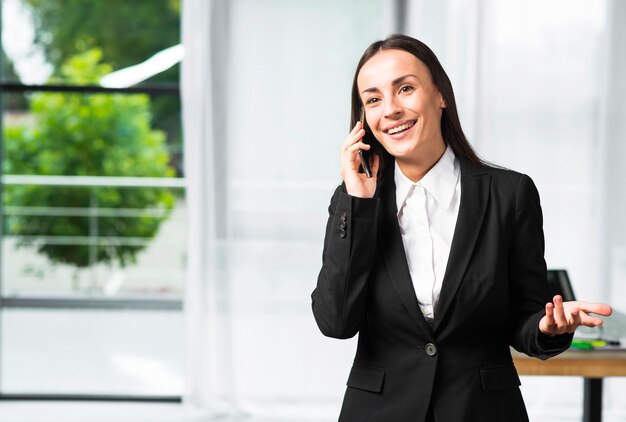 Empresaria joven sonriente que toma en gesticular del teléfono móvil