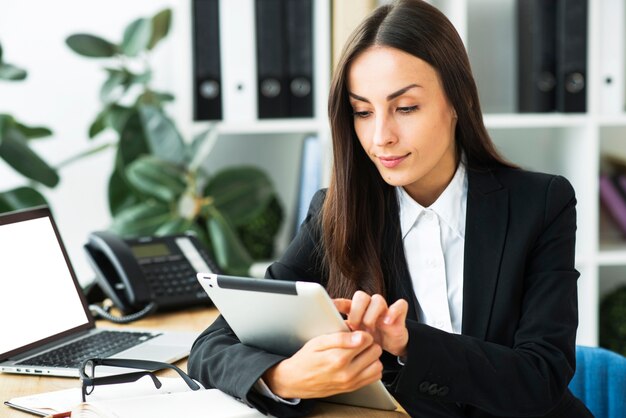 Empresaria joven sonriente que usa la tableta digital en la oficina