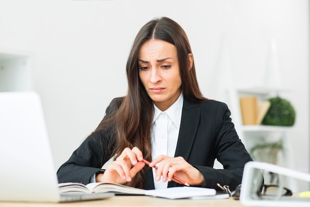 Empresaria joven triste que sostiene el lápiz rojo en su mano que se sienta en el escritorio de oficina
