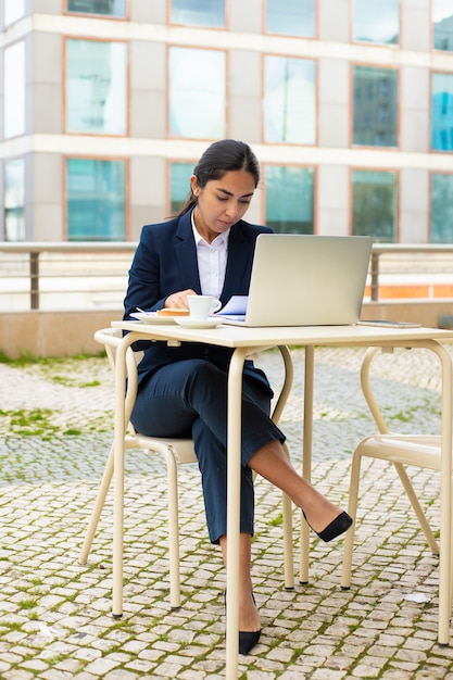 Empresaria con laptop y papeles en café