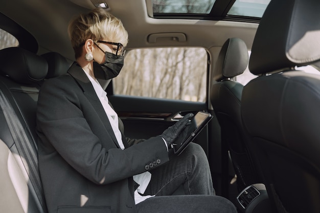 Foto gratuita empresaria en una máscara negra sentada dentro de un automóvil