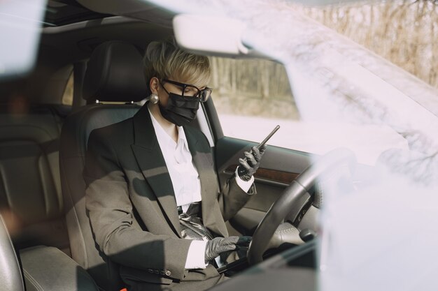 Empresaria en una máscara negra sentada dentro de un automóvil