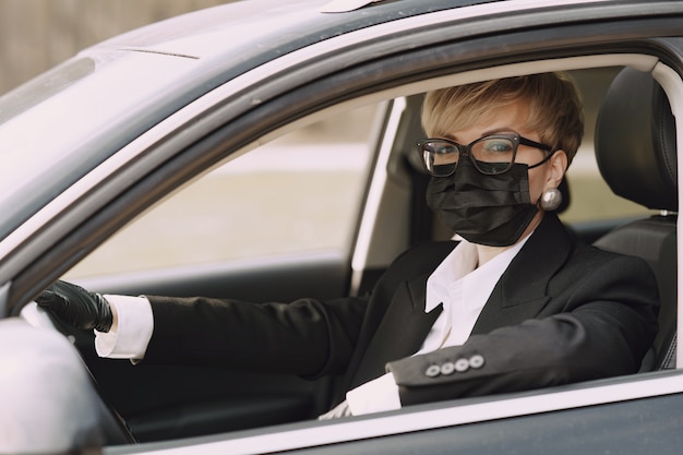 Empresaria en una máscara negra sentada dentro de un automóvil