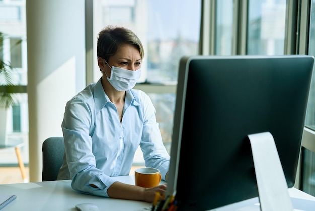 Empresaria con mascarilla mientras trabaja en una PC de escritorio en la oficina