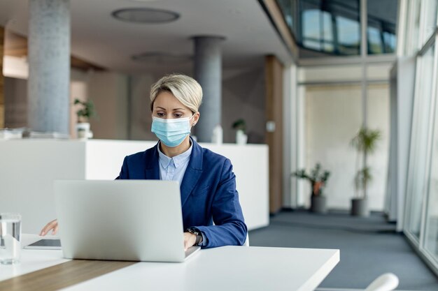 Empresaria con mascarilla protectora trabajando en una laptop en la oficina