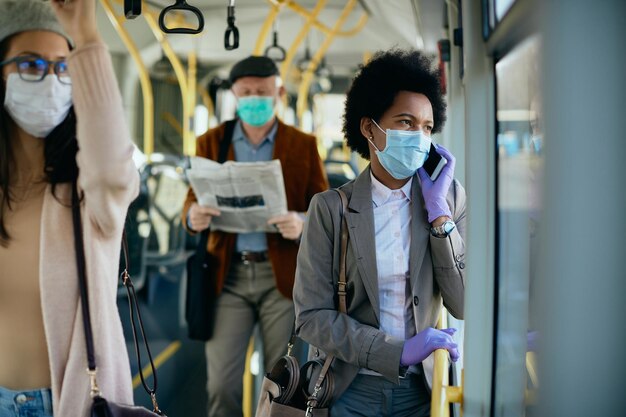 Empresaria negra con mascarilla hablando por teléfono en un transporte público