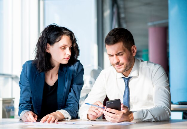 Empresaria que mira al hombre que usa smartphone