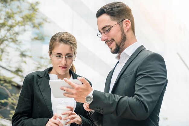 Empresaria que mira el asimiento del smartphone por un hombre de negocios joven sonriente