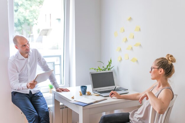 Empresaria que mira a su socio que sostiene la tableta digital gráfica en oficina