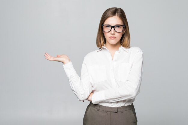 Empresaria que muestra el espacio de la copia para el producto con la palma de la mano abierta. Sonriente expresión amistosa en la joven empresaria con gafas aisladas en la pared blanca.