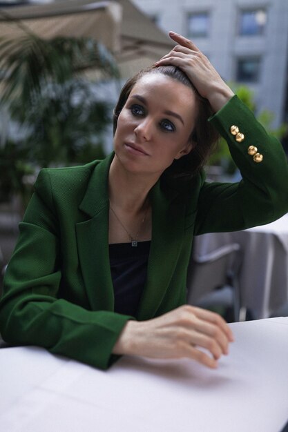 Empresaria sentada en la cafetería y descansar un poco después de todas las reuniones y entrevistas. Elegante chaqueta verde y blusa negra, corte de pelo corto, maquillaje nude.