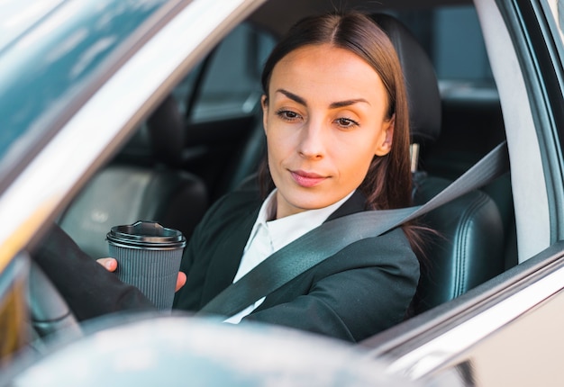 Empresaria sentada dentro del asiento de auto sosteniendo una taza de café desechable