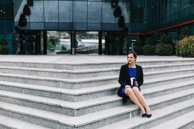 Empresaria sentada en la escalera frente a la entrada del edificio