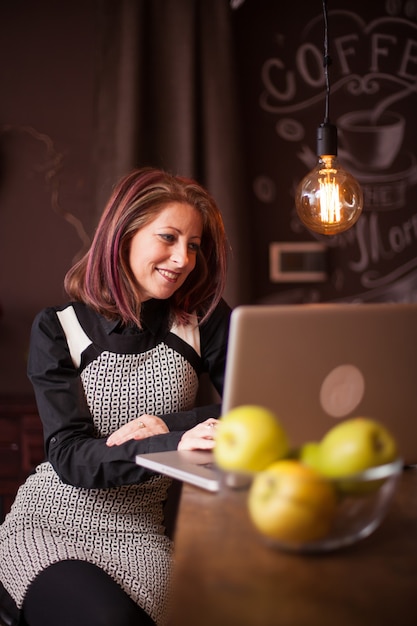 La empresaria sonriendo mientras mira su computadora portátil en una cafetería vintage. Disfrutando sentada en la barra del bar