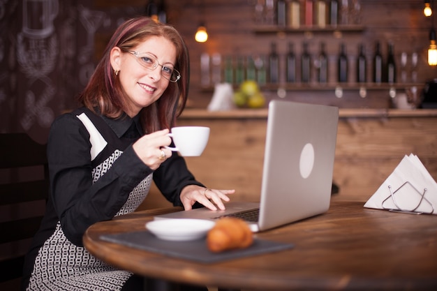 Empresaria sonriendo mientras toma una taza de café. Beber café en una cafetería vintage