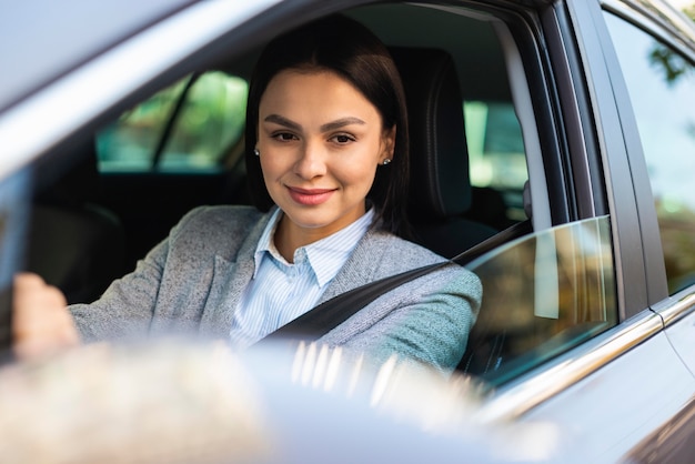 Empresaria sonriente conduciendo su coche y mirando en el espejo lateral