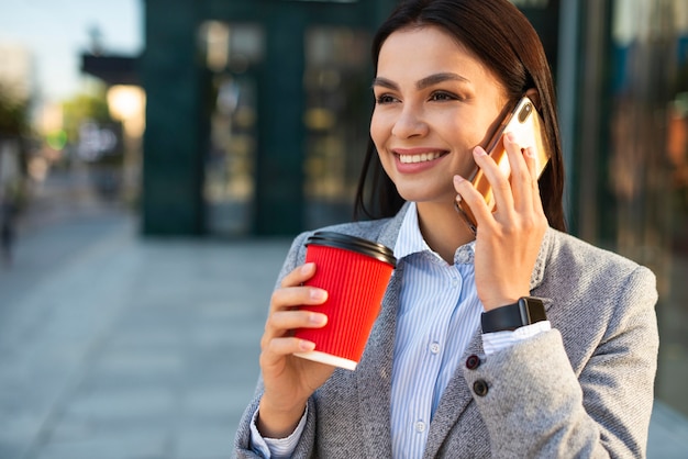 Empresaria sonriente hablando por teléfono mientras toma un café en la ciudad