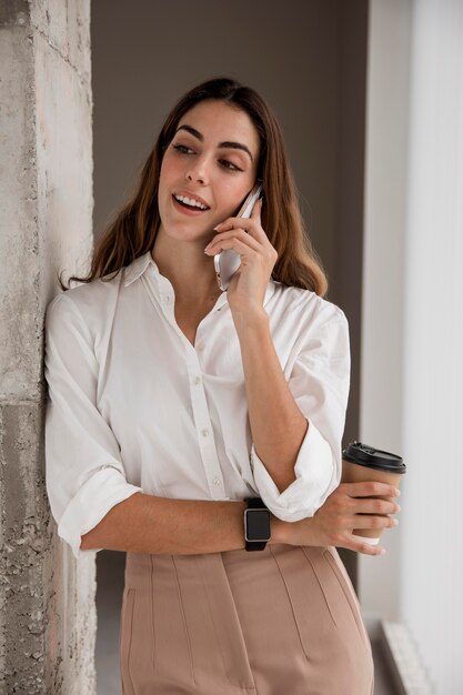 Empresaria sonriente hablando por teléfono mientras toma un café