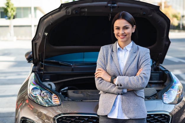 Empresaria sonriente posando junto al coche con capó abierto