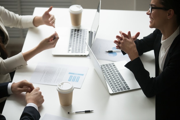 Empresaria sonriente que disfruta de hablar con los colegas durante trabajo en equipo con las computadoras portátiles