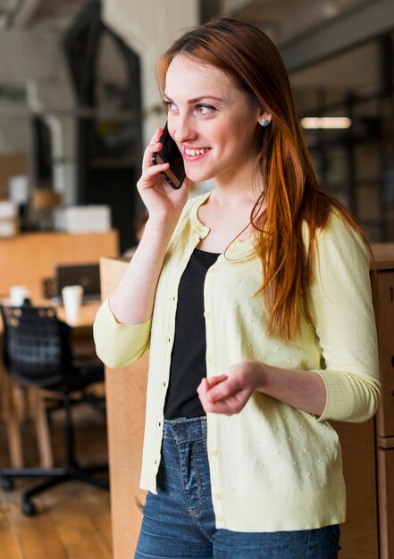 Empresaria sonriente que habla en smartphone en oficina