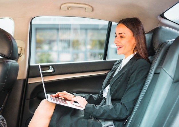 Empresaria sonriente que se sienta dentro del coche usando el ordenador portátil