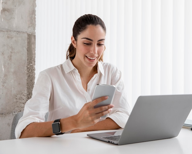 Empresaria sonriente con smartphone y portátil