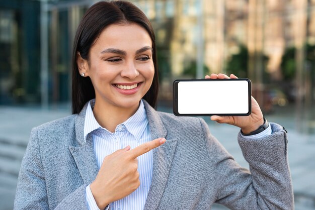 Empresaria sonriente sosteniendo y apuntando al teléfono inteligente