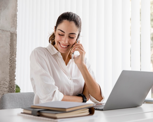 Empresaria sonriente trabajando con smartphone y portátil