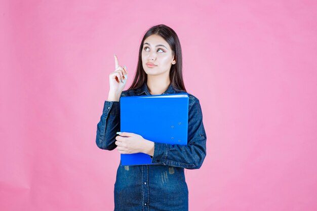 La empresaria sosteniendo una carpeta de informe azul y apuntando hacia arriba