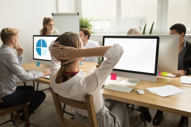 Empresaria sosteniendo las manos detrás de la cabeza descansando el trabajo de acabado, vista trasera