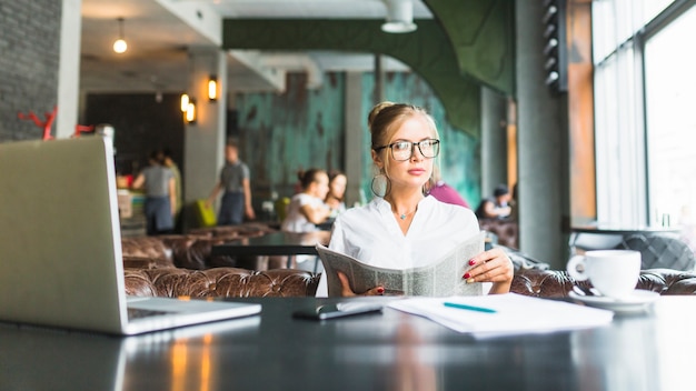 Foto gratuita empresaria sosteniendo el periódico sentado en el restaurante