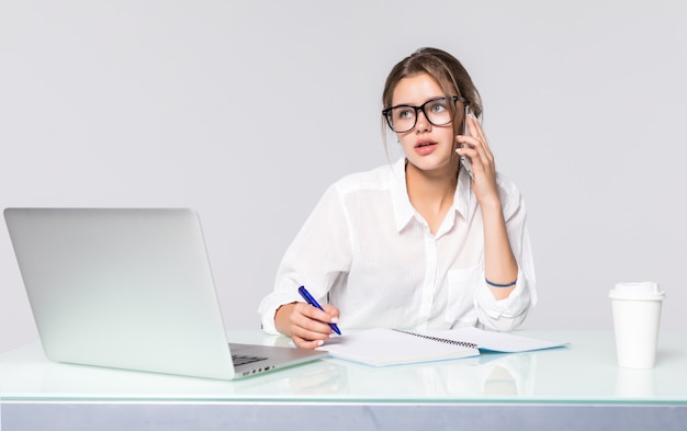 Empresaria en su escritorio de trabajo con ordenador portátil y teléfono parlante aislado sobre fondo blanco.