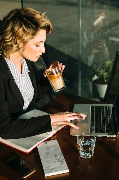 Empresaria tomando un batido de chocolate mientras usa una computadora portátil en un restaurante