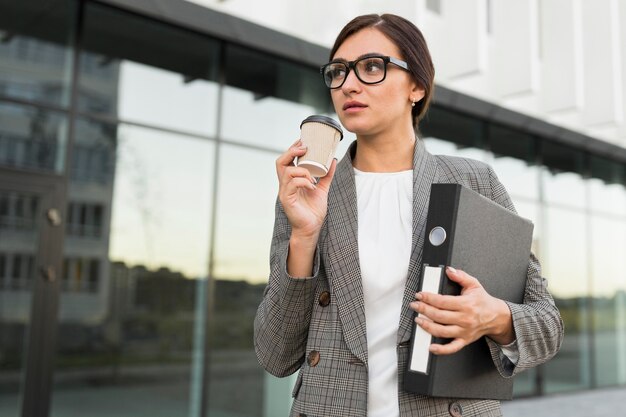 La empresaria tomando un café al aire libre mientras sostiene binder