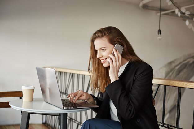 La empresaria trabajando en la cafetería, hablando por teléfono y mirando portátil