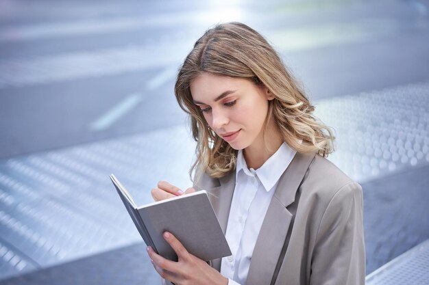 La empresaria en traje corporativo escribe algo sobre ideas en un cuaderno que se encuentra afuera en el centro de la ciudad