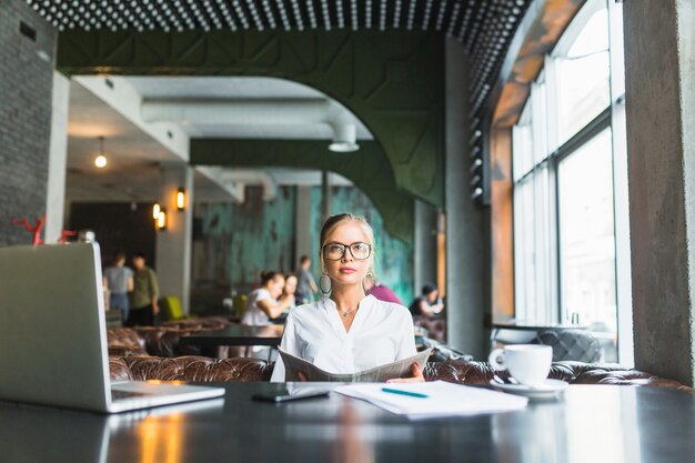 Empresaria usando gafas con periódico en café