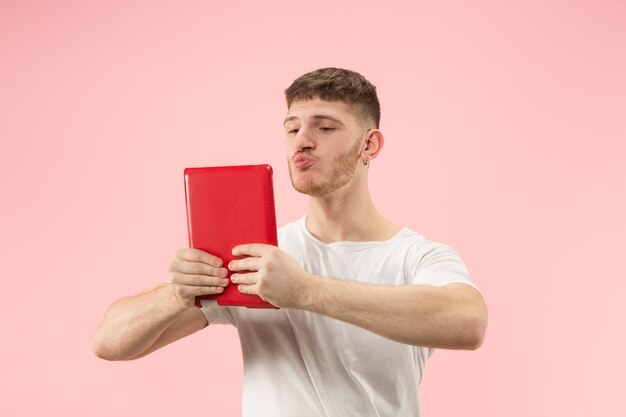 Empresario abrazando portátil. Amor al concepto de computadora. Retrato frontal de medio cuerpo masculino atractivo, fondo de color rosa moderno de estudio. Joven barbudo emocional. Las emociones humanas, el concepto de expresión facial.