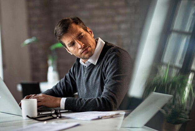 Empresario adulto medio que trabaja en una computadora y mira hacia otro lado mientras se siente insatisfecho con algo