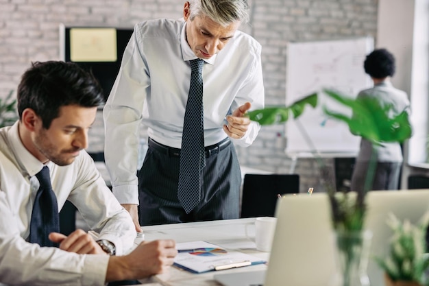 Empresario adulto medio revisando papeleo y leyendo estadísticas de proyectos mientras trabaja en la oficina