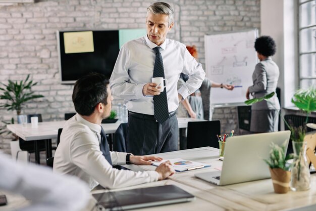 Empresario adulto medio y su joven colega hablando mientras analizan las estadísticas comerciales en el trabajo