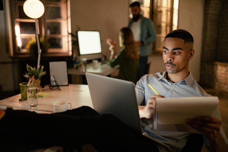 Foto gratuito empresario afroamericano escribiendo informes mientras trabaja hasta tarde en una computadora en la oficina