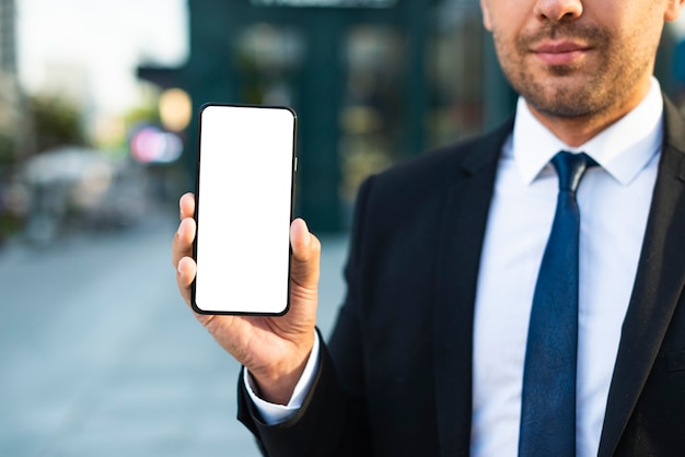 Empresario al aire libre sosteniendo un teléfono móvil vacío