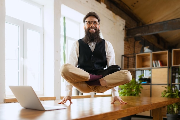 Empresario alegre empleado de pie en pose de yoga en la oficina en la mesa de trabajo meditando después del trabajo