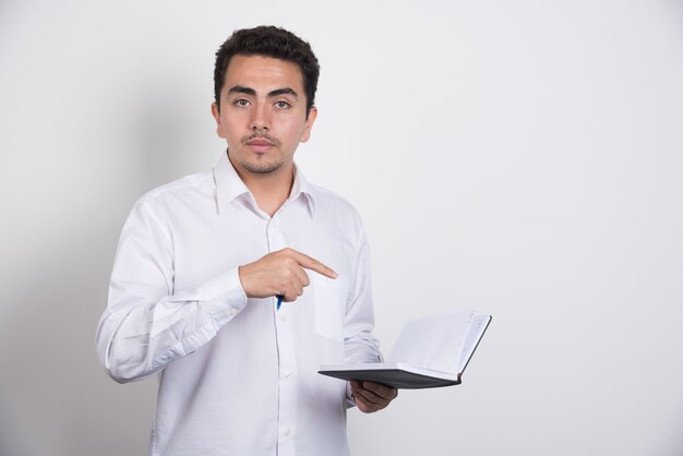 Empresario apuntando al cuaderno sobre fondo blanco.