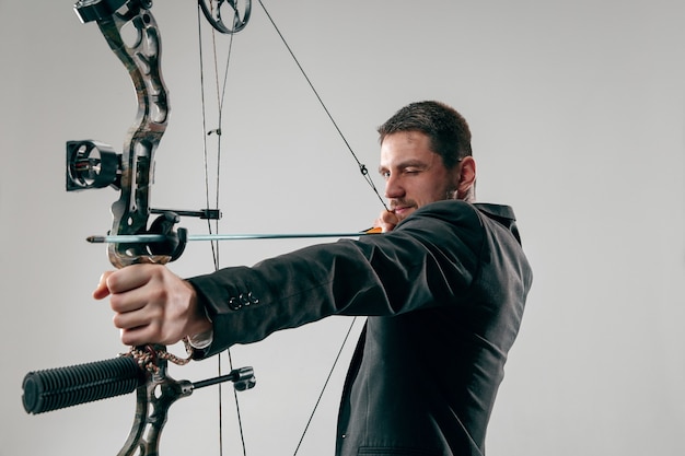 Foto gratuita empresario apuntando al objetivo con arco y flecha, aislado en la pared gris del estudio